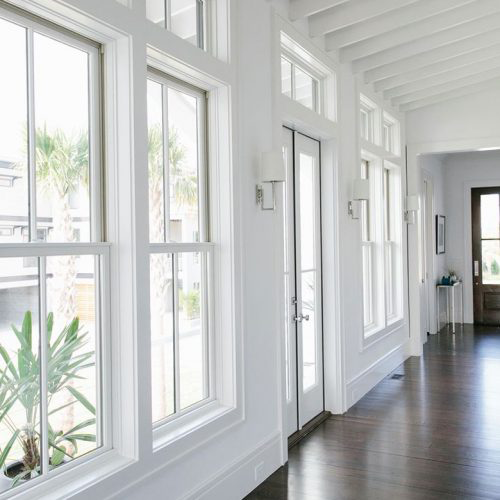 Bright interior hallway with white-trimmed windows and a glass door looking out toward palm trees.