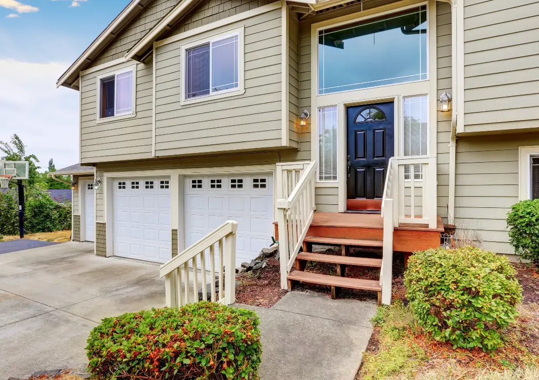 Two-story beige house with a black front door, small porch, and two white garage doors.