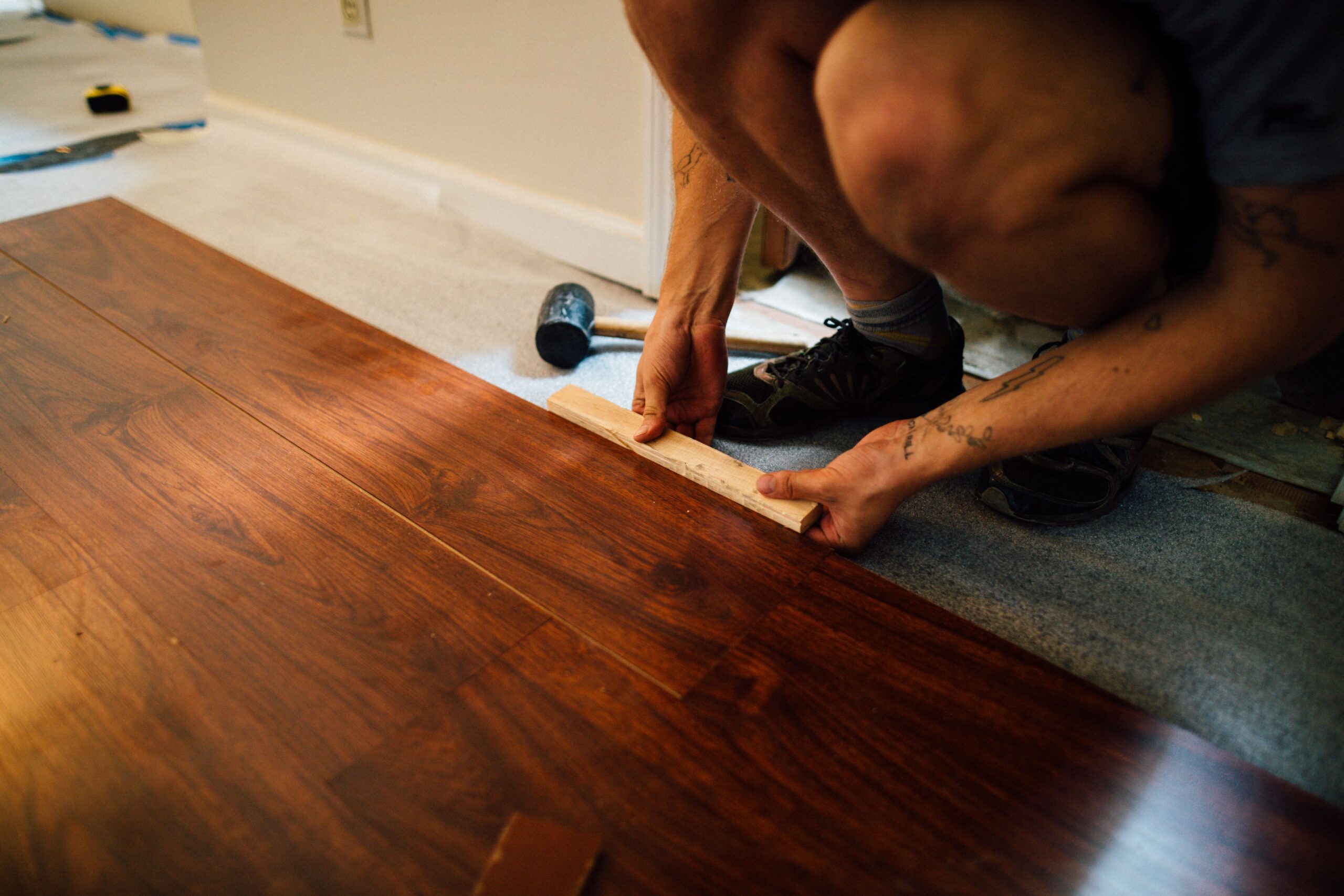 Faceless male master laying wooden laminate flooring using mallet in apartment during renovation